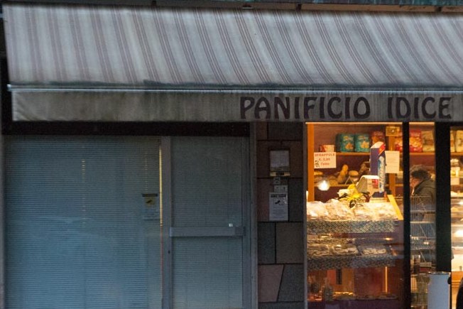 La facciata del Panificio Idice in Via del Fiume: il tendone a righe, l'insegna dipinta e la vetrina illuminata la sera.